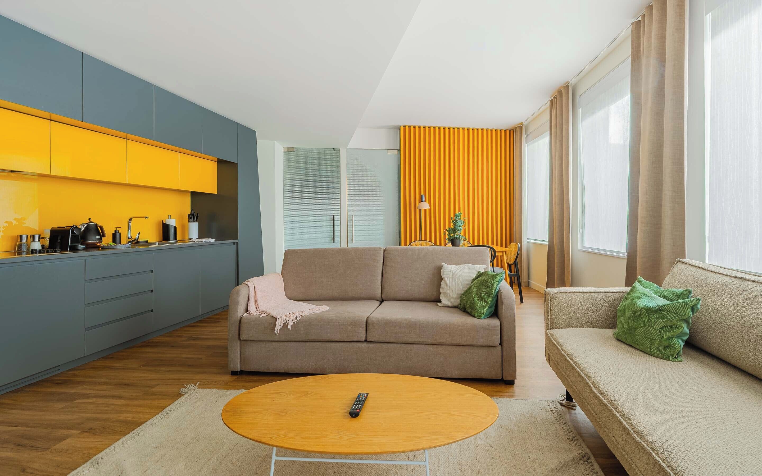 A modern living room with a sofa, a coffee table, and a kitchen area with yellow cabinets.