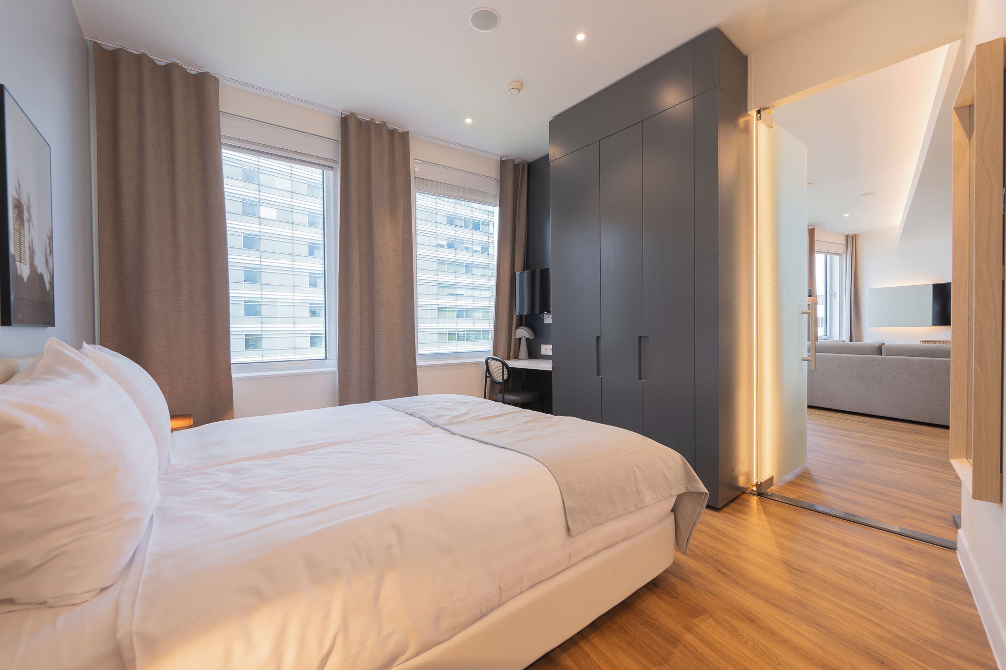 A modern bedroom with a large bed, a desk, and a wardrobe.