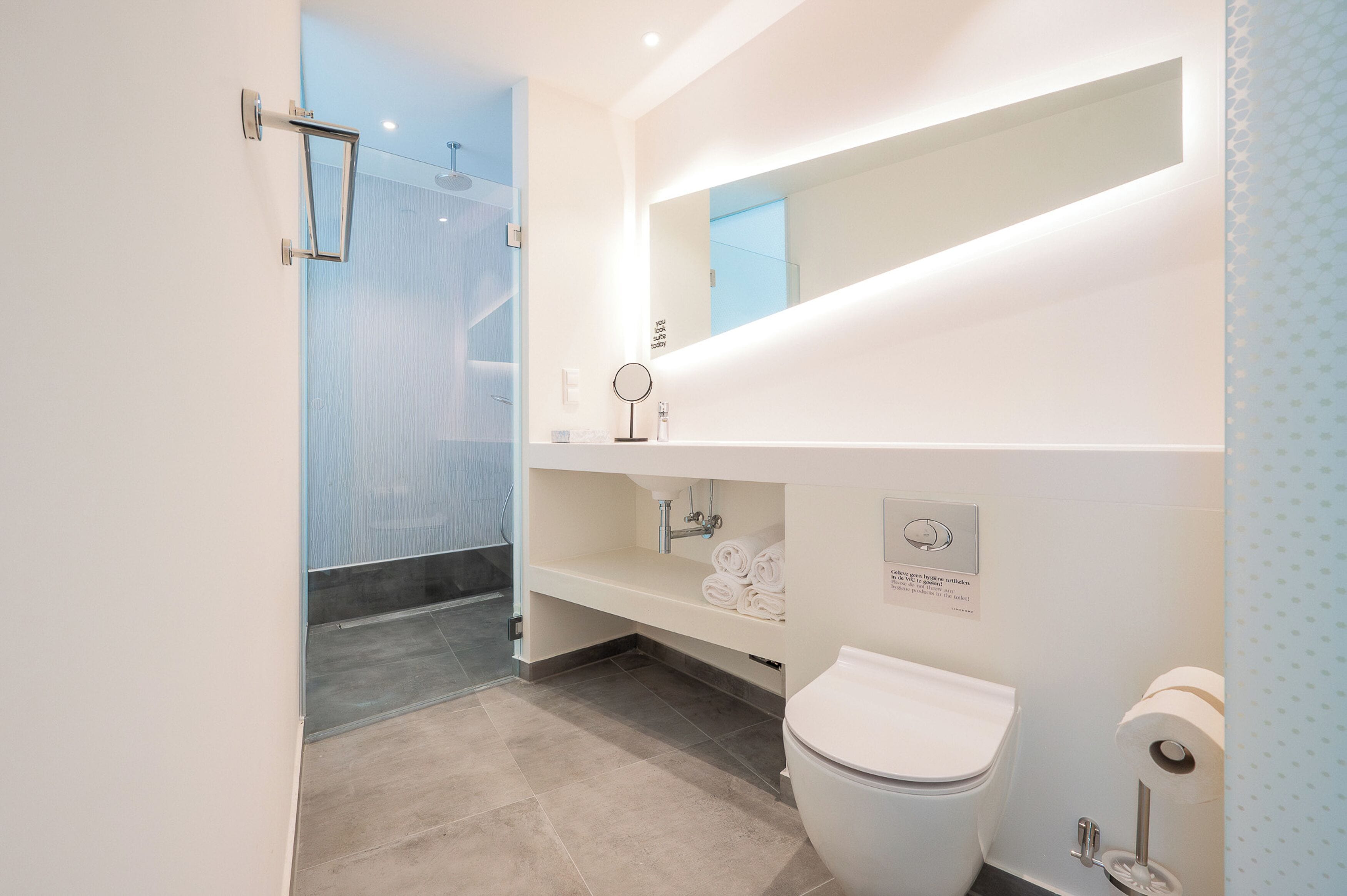 Un baño moderno con cabina de ducha de vidrio, inodoro, lavabo con espejo y toallero.