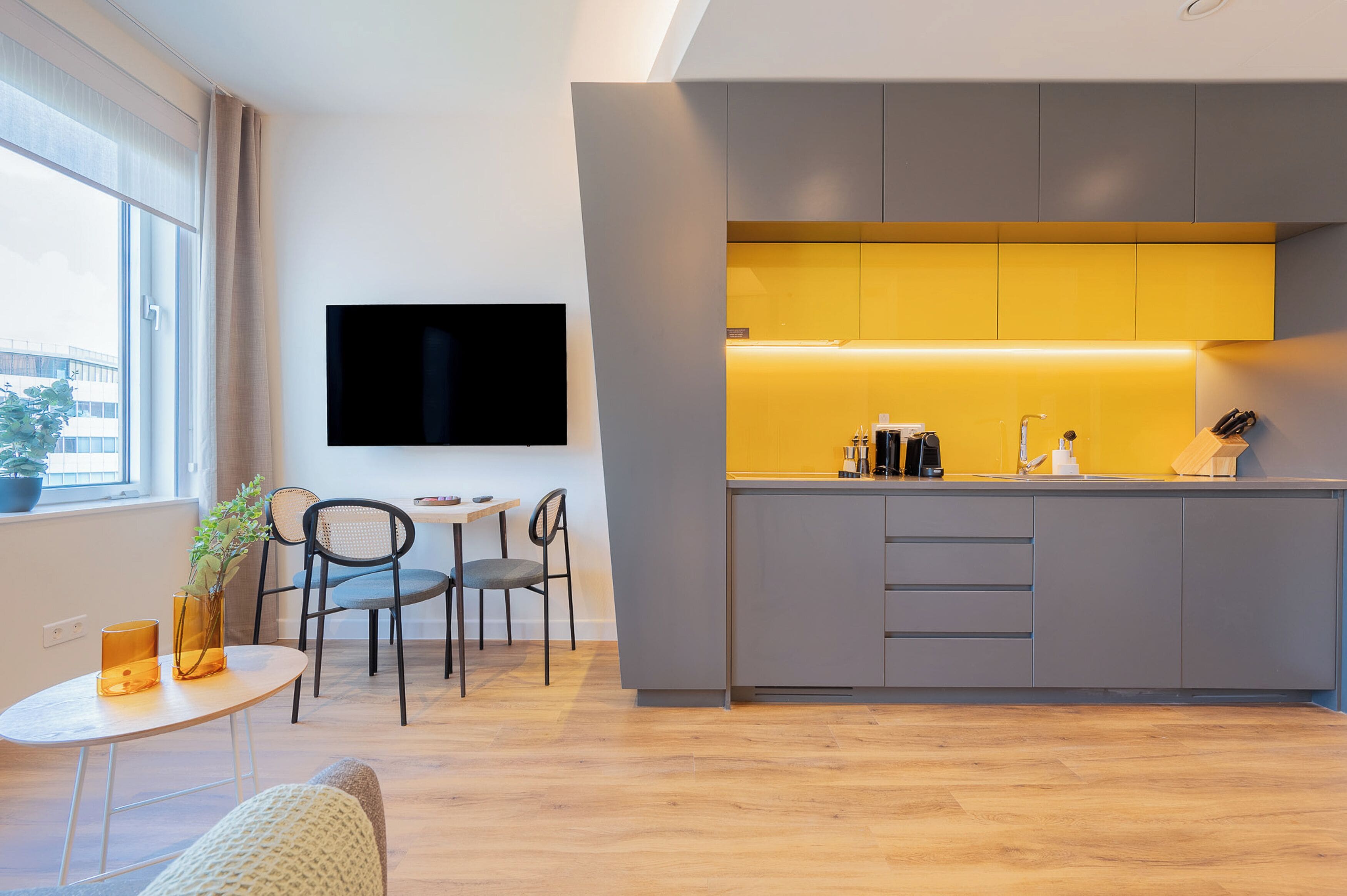 A modern kitchen with a built-in island, a flat-screen TV mounted on the wall, and a dining area with a small table and chairs.