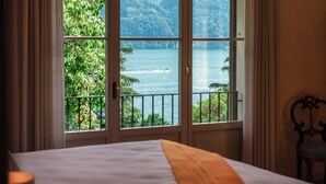 A hotel room with a large window offering a view of a lake and mountains.