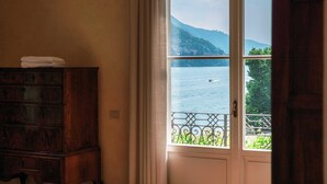 A room with a view of a lake and mountains through a window with a metal railing.
