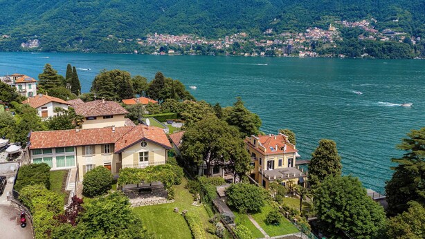 A lakeside village with traditional houses, a clear view of the lake, and mountains in the background.