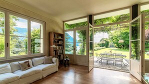A spacious living room with a large window, a sofa, a bookshelf, and a patio area with a table and chairs.