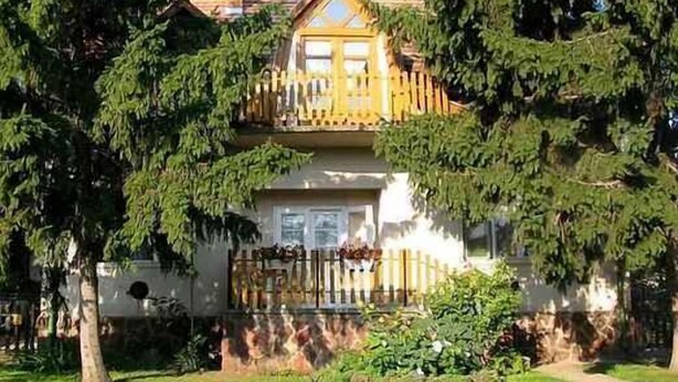 Una casa de dos pisos con balcón, rodeada de árboles.