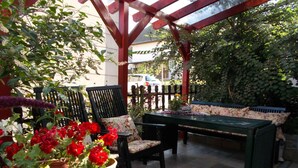 Un patio exterior con una mesa y sillas de madera, rodeado de macetas con plantas y una valla de madera.