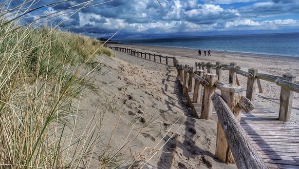 A beach with a wooden boardwalk leading to the shore, sandy dunes, and a cloudy sky. - Victoria Guest Accommodation & Studio Apartments (Pwllheli)