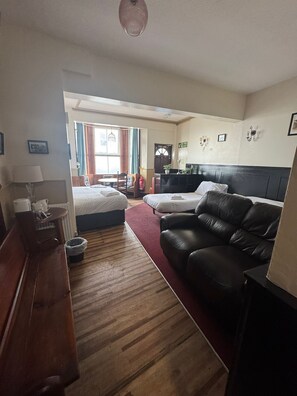 Hotelkamer met houten vloer, een zwarte leren bank, een bed, een bureau met een lamp en uitzicht op buiten.