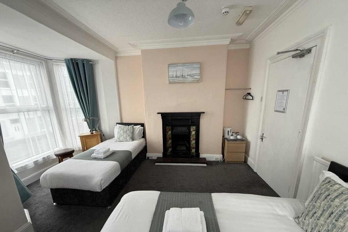 A hotel room with two beds, a fireplace, a window with curtains, and a door with a coat rack.