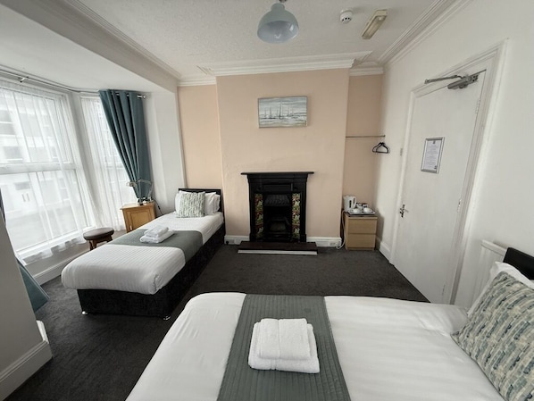 Ett hotellrum med två sängar, en öppen spis, ett fönster med gardiner och en dörr med en klädhängare.