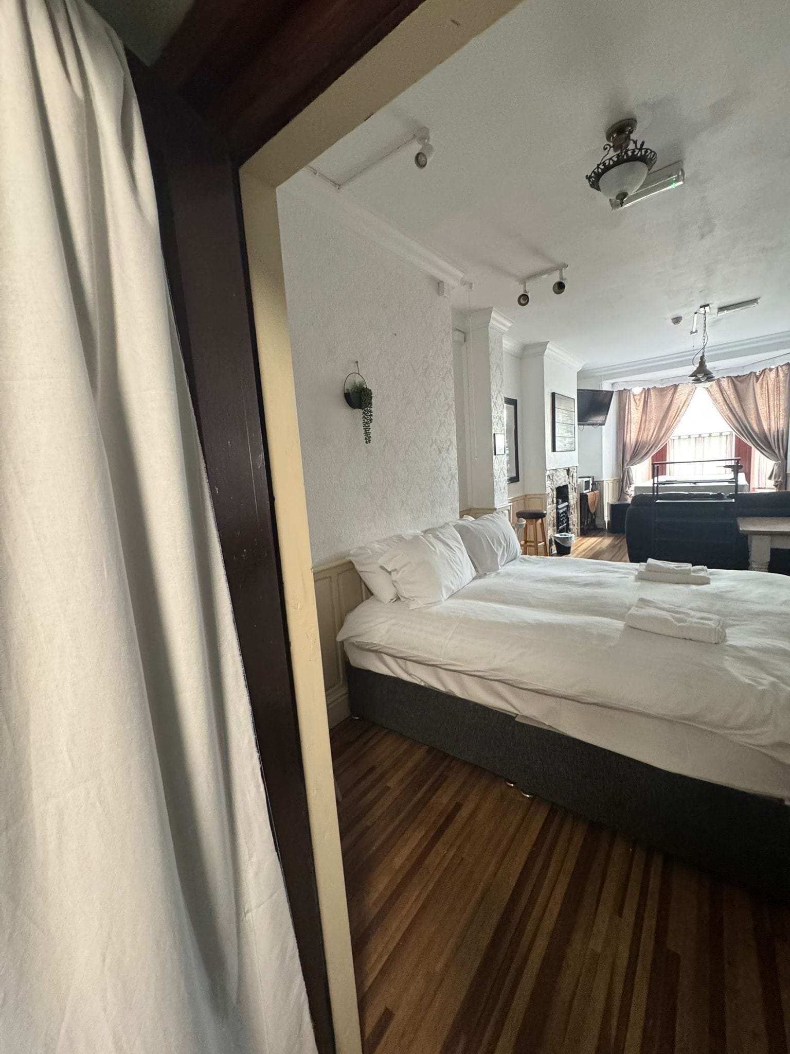A hotel room with a large bed, a ceiling fan, a window with curtains, and a small plant on the wall.