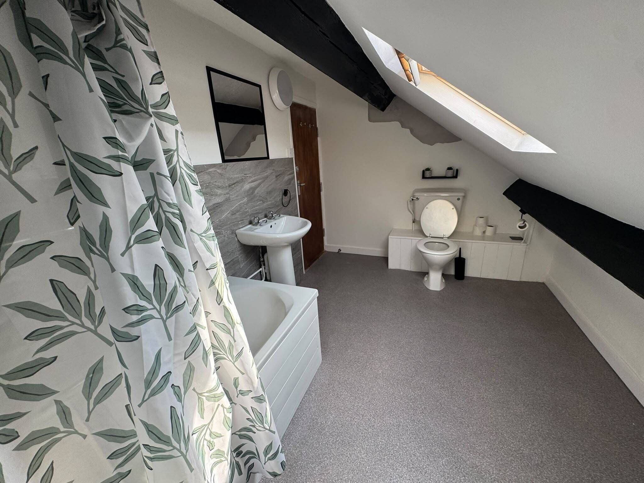 A bathroom with a bathtub, sink, toilet, and a shower curtain with a leaf pattern.