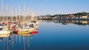 A marina with various boats docked, calm water, and a distant view of a town with buildings and hills. - Victoria Guest Accommodation & Studio Apartments (Pwllheli)