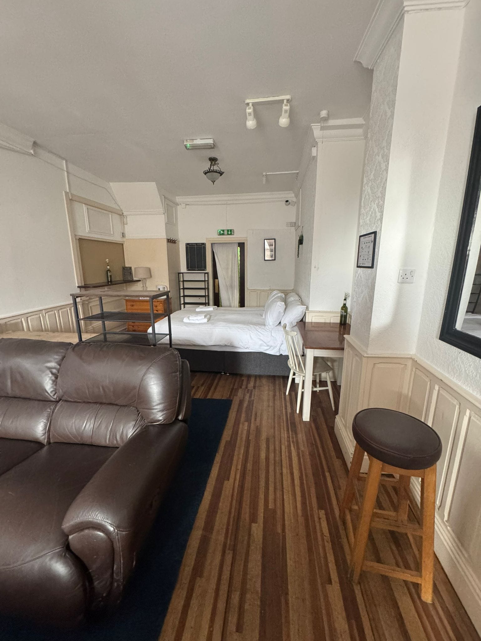 A room with a bed, a brown leather sofa, a wooden stool, and a small table.