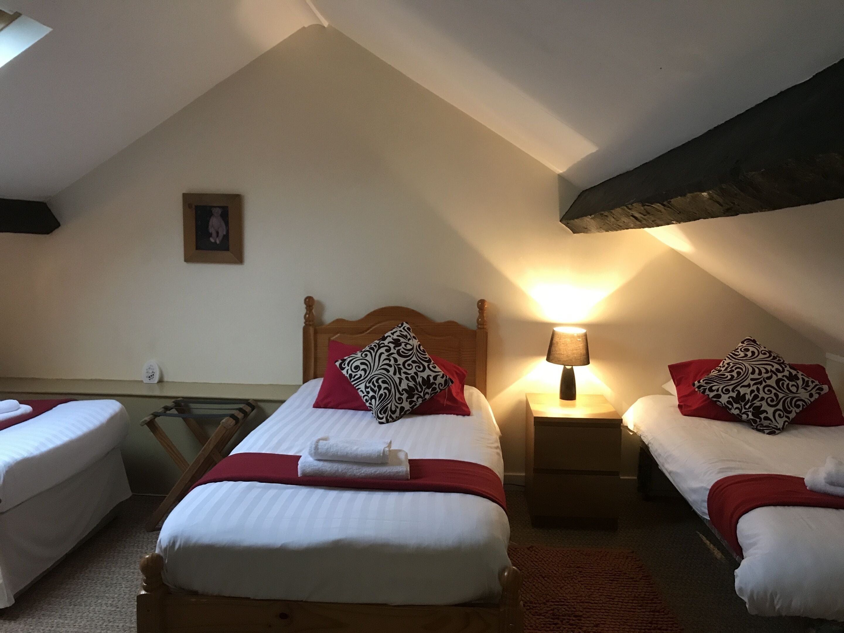 Habitación de hotel con dos camas, cabecero de madera, lámpara de noche y una manta roja.
