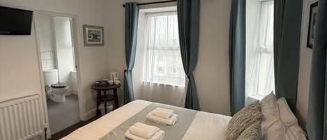 A neatly made bed with towels, a bedside table, a lamp, and a window with curtains.