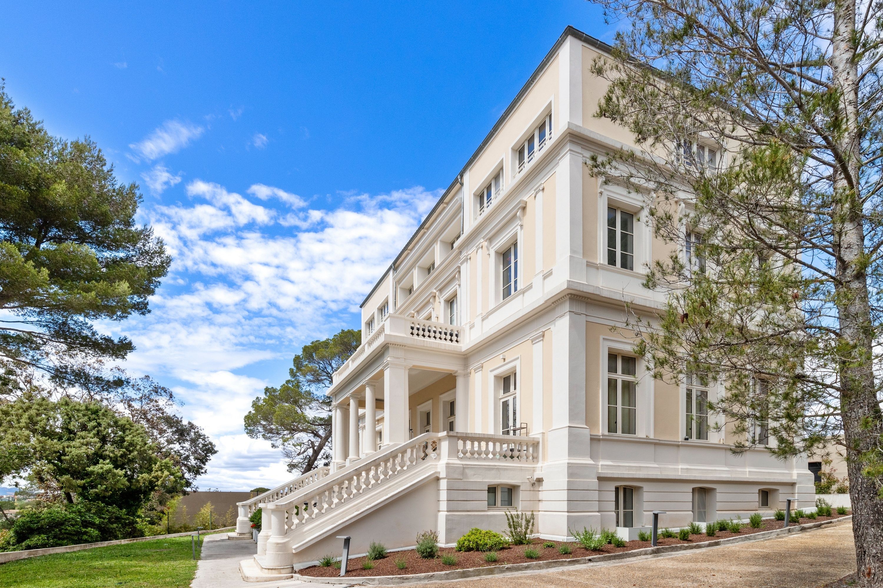 A large, multi-story building with a grand entrance, a staircase, and a well-maintained lawn.