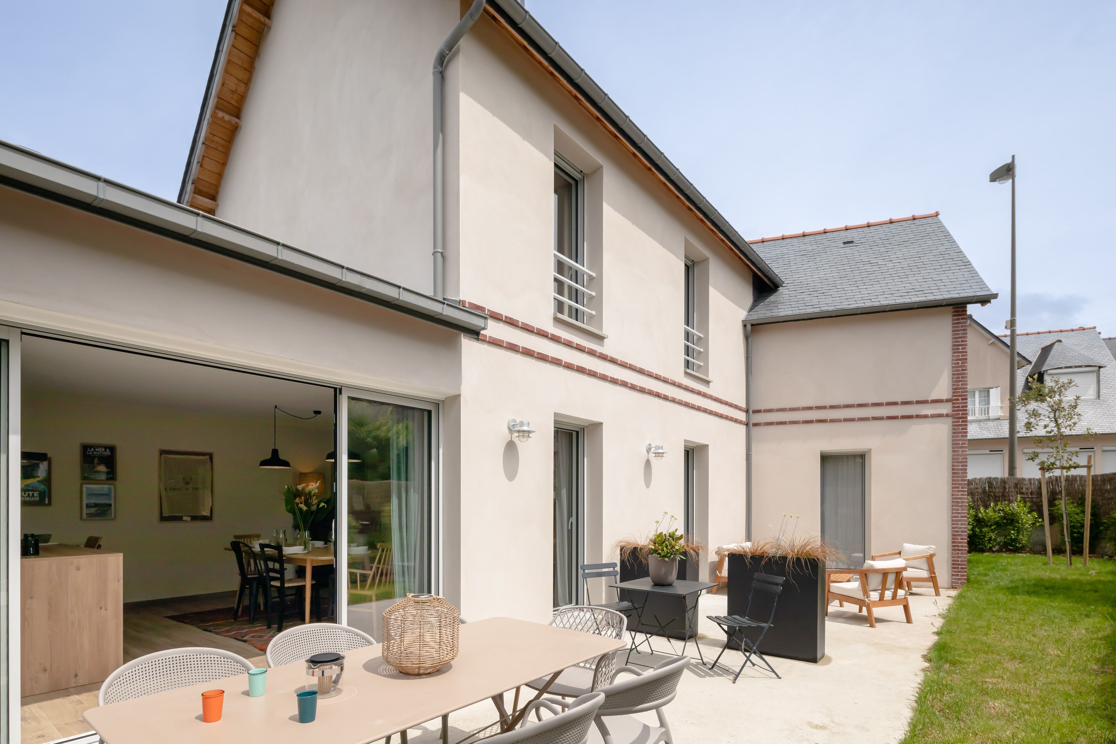 Une maison moderne dotée d’un patio comprenant une table et des chaises, une chaise d’extérieur noire et une plante en pot.