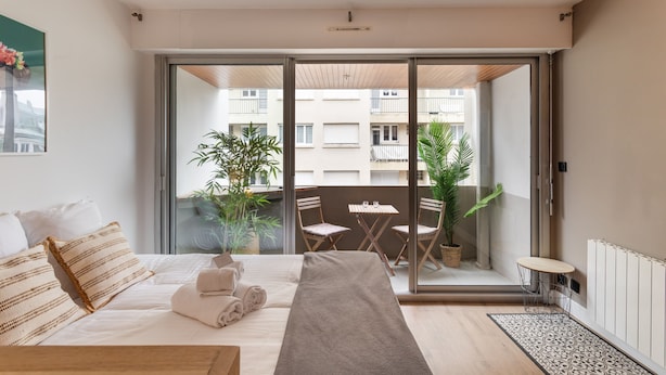 Une chambre moderne avec un grand lit, une petite table et un balcon agrémenté de plantes et d’une table.