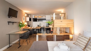 Une chambre d’hôtel compacte comprenant un lit, un bureau, une kitchenette et un téléviseur fixé au mur.