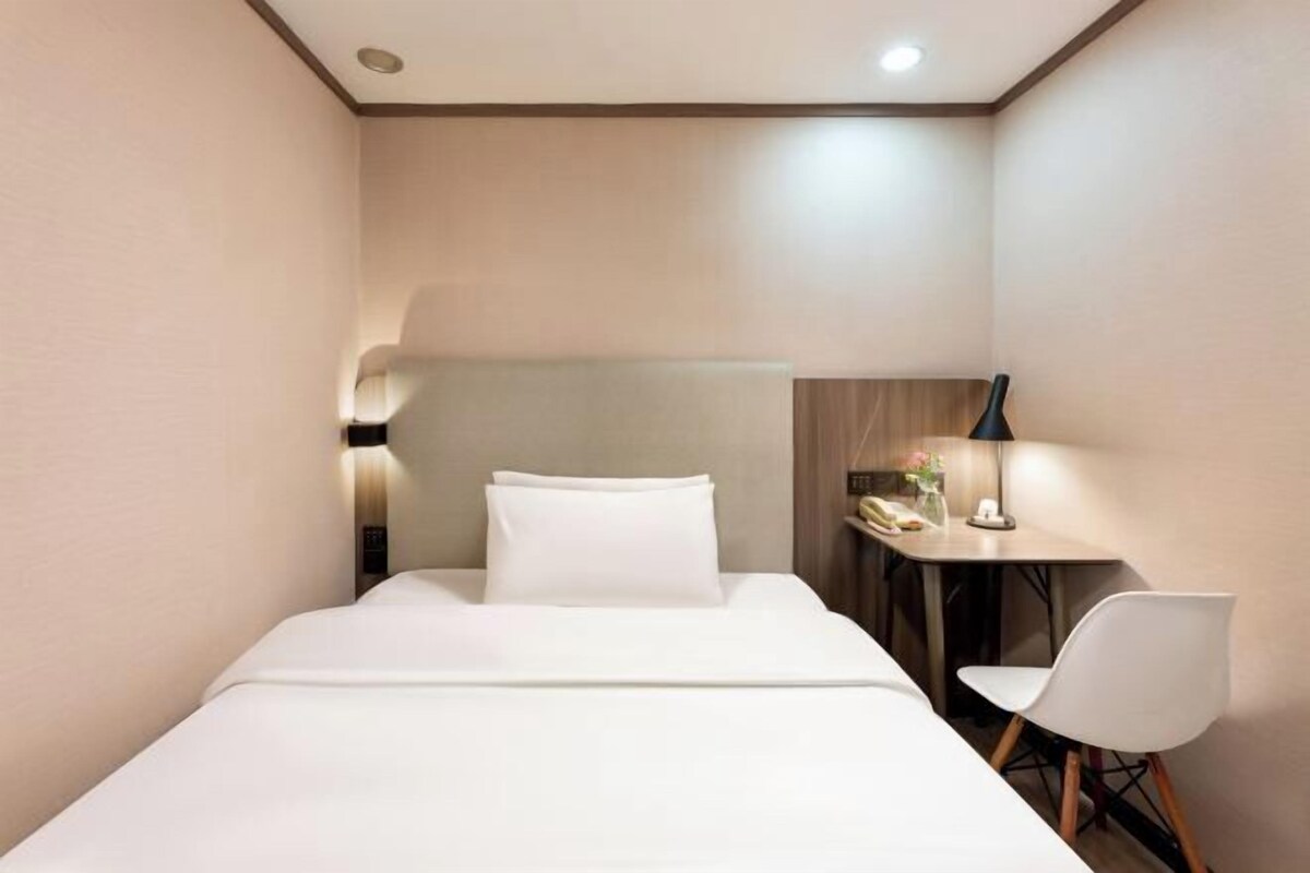 A hotel room with a bed, a desk with a chair, and a lamp.