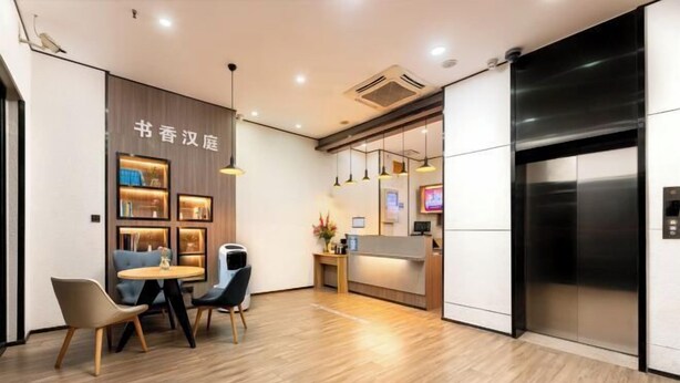 A modern hotel lobby with a reception desk, a seating area with chairs, a wooden floor, and an elevator. - Hilbert Hotel (Guangzhou Nansha Wanda Plaza Jinzhou Subway Station) (Guangzhou)