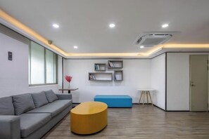 A modern living room with a sofa, a round coffee table, and a blue sofa. There are shelves with books and a vase with flowers. - Hilbert Hotel (Guangzhou Nansha Wanda Plaza Jinzhou Subway Station) (Guangzhou)