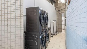 A laundry room with stacked washers and dryers, a tiled floor, and a metal rack. - Hilbert Hotel (Guangzhou Nansha Wanda Plaza Jinzhou Subway Station) (Guangzhou)
