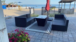 En terrasse med fletmøbler, en rød parasol og udsigt til stranden.