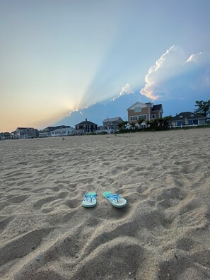Ein Paar Flip-Flops am sandigen Strand, im Hintergrund Häuser.