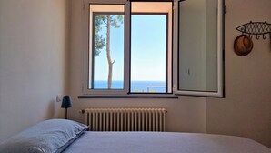 Une chambre à coucher avec un lit, une fenêtre donnant sur la mer, un radiateur et un luminaire fixé au mur.