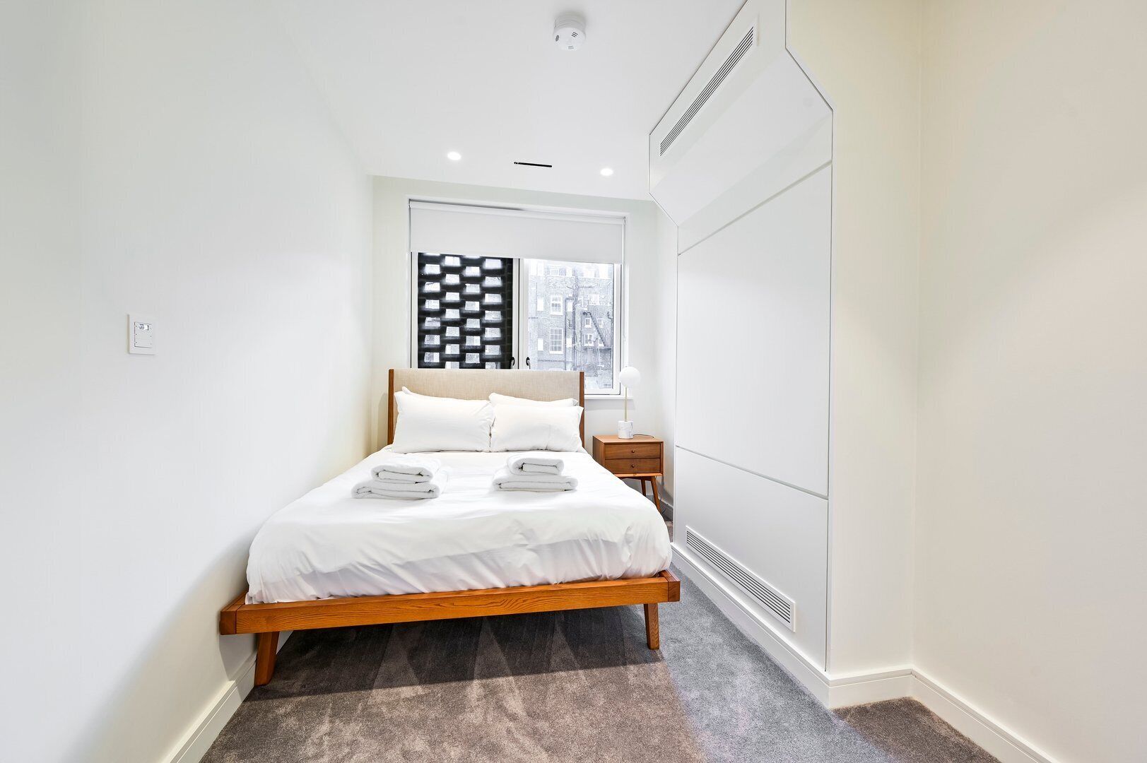 Une chambre moderne avec un lit, une table de chevet, une fenêtre donnant sur un beau paysage et une armoire intégrée.