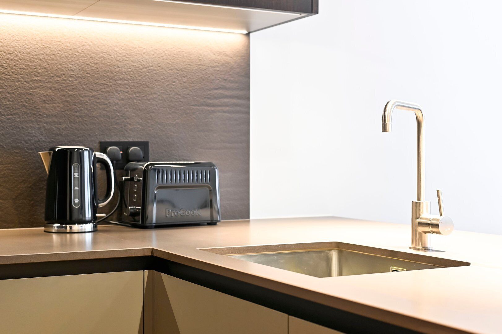 Une cuisine moderne avec un évier élégant en acier inoxydable, un grille-pain noir de la marque ProCook et une bouilloire posée sur le plan de travail.