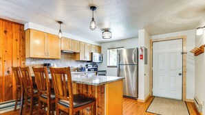 A kitchen with wooden cabinets, a central island with chairs, stainless steel appliances, and pendant lighting. - Winter Park Condo w/ Resort Shuttle On-Site! (Winter Park)