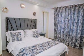 Een net opgemaakt bed met een grijs hoofdeinde, wit beddengoed en gestreepte kussens.