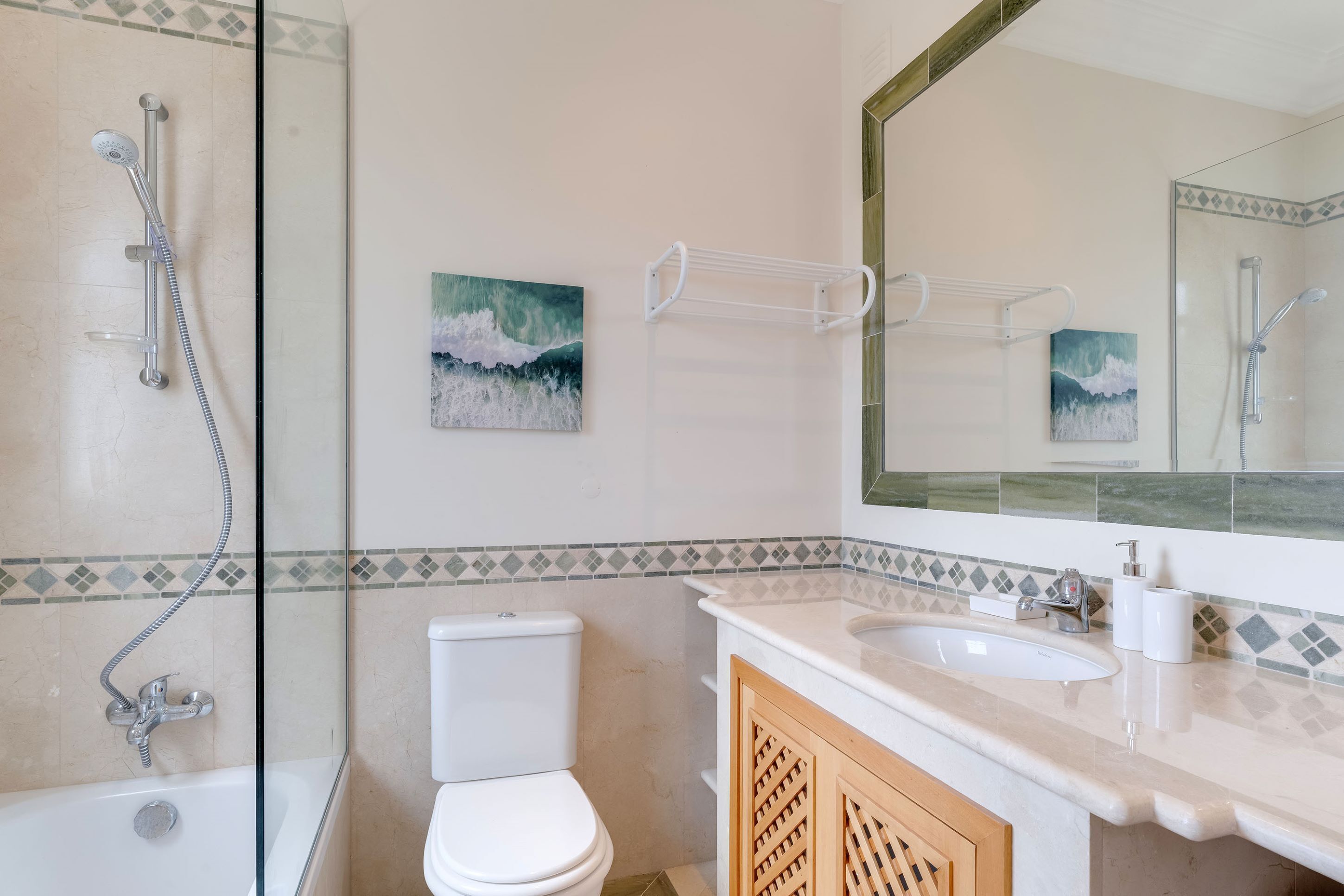 A bathroom with a glass-enclosed shower, a toilet, a sink with a mirror, and decorative tiles.