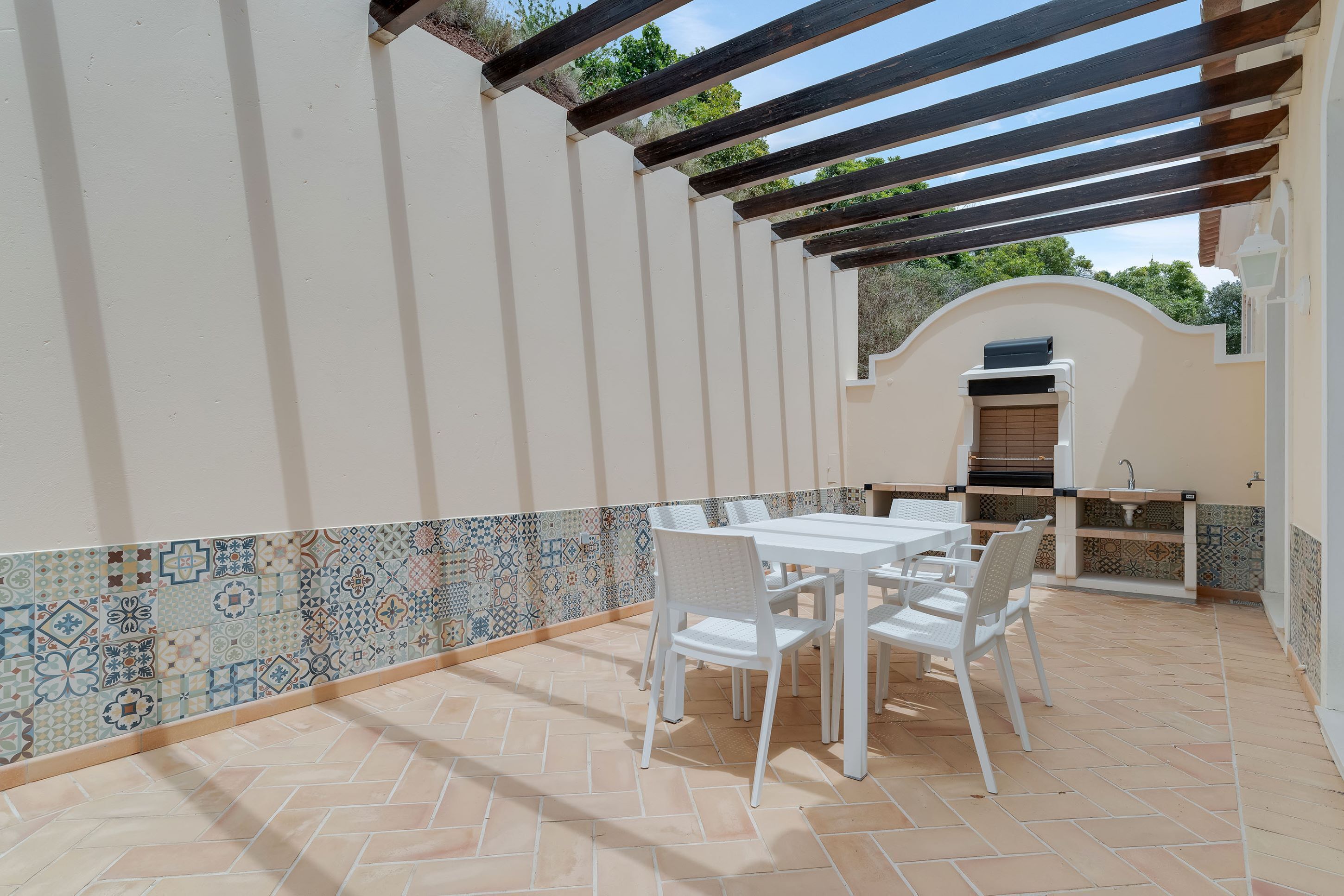 An outdoor patio with a tiled floor, a white table with chairs, and a grill area.