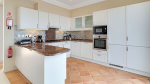 A modern kitchen with white cabinets, a central island, a microwave, and an oven. - Villa Sol Palheiro Village (Funchal)