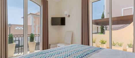 A hotel room with a large bed, a television mounted on the wall, and a balcony with potted plants.