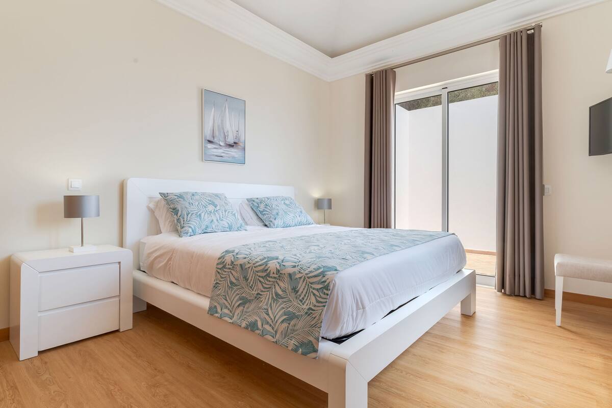 A modern bedroom with a bed, bedside tables, a bench, and a painting on the wall.