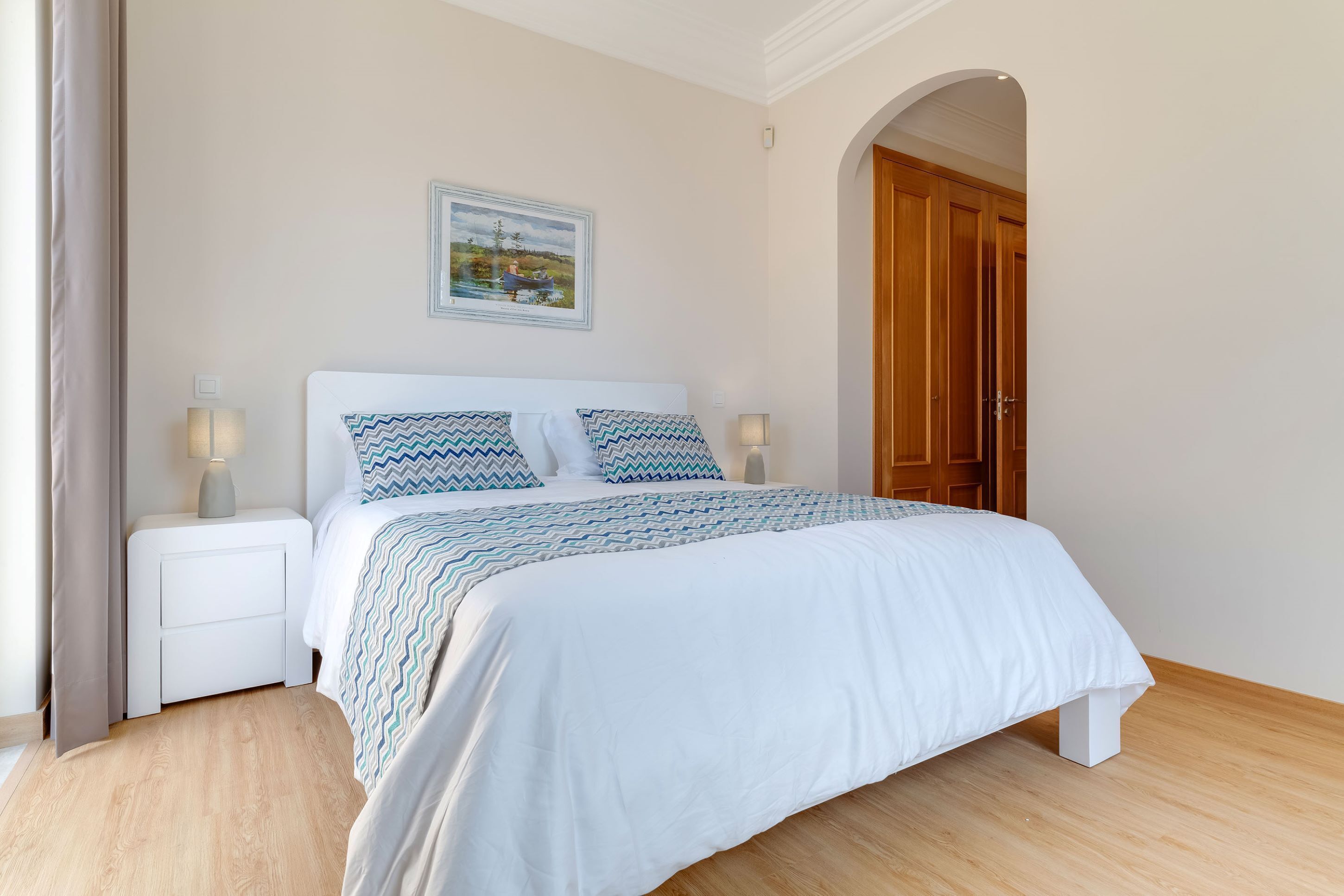 A bedroom with a bed, nightstands, a painting, and a wooden door.