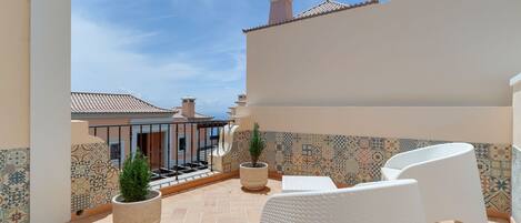A terrace with tiled flooring, white wicker furniture, and potted plants.