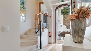 A staircase with a wooden handrail, a fire extinguisher, and a decorative vase with flowers. - Villa Sol Palheiro Village (Funchal)