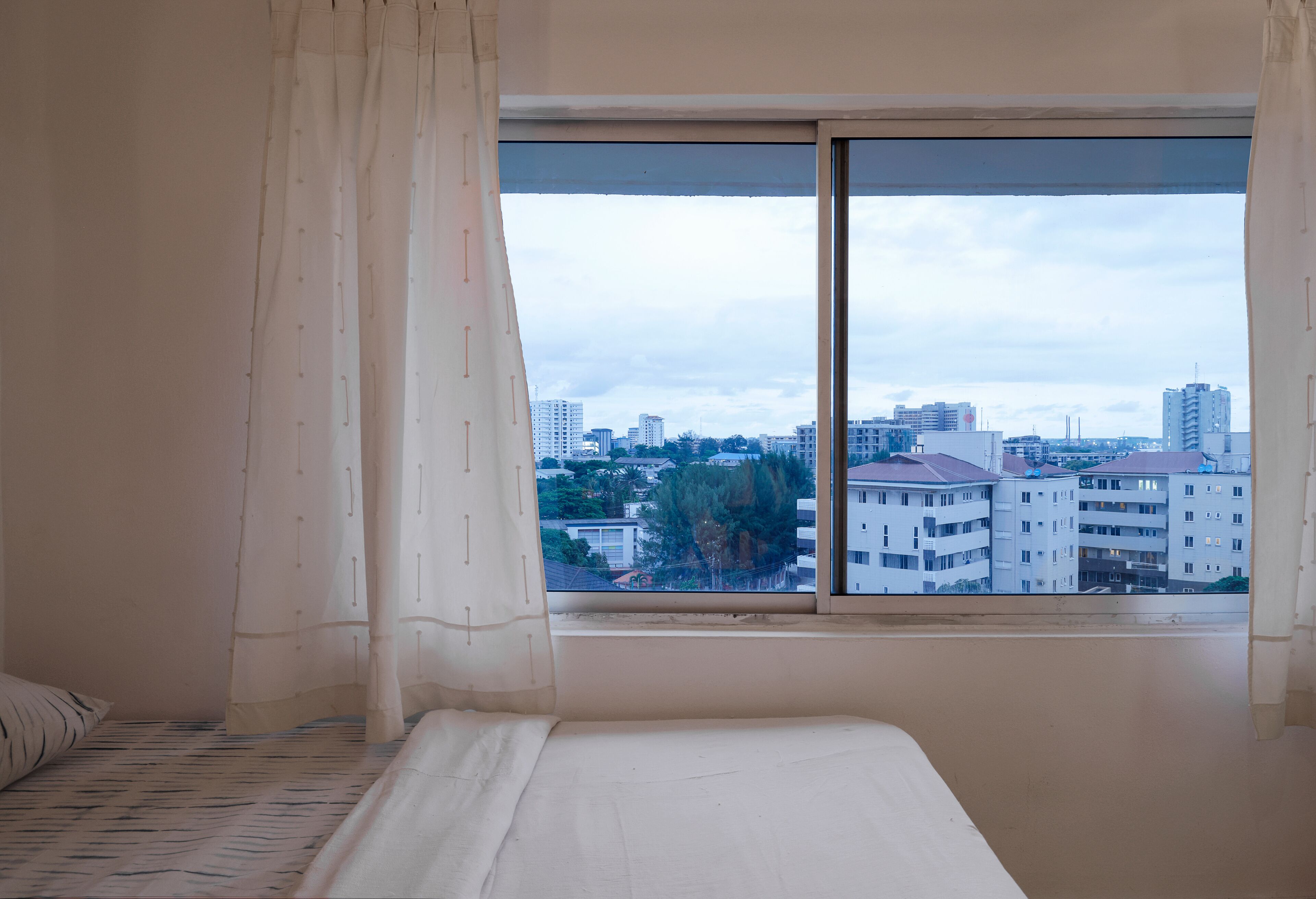 Un dormitorio con un ventanal grande, una cama y vistas a un paisaje urbano.