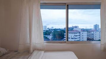 Un dormitorio con un ventanal grande, una cama y vistas a un paisaje urbano.