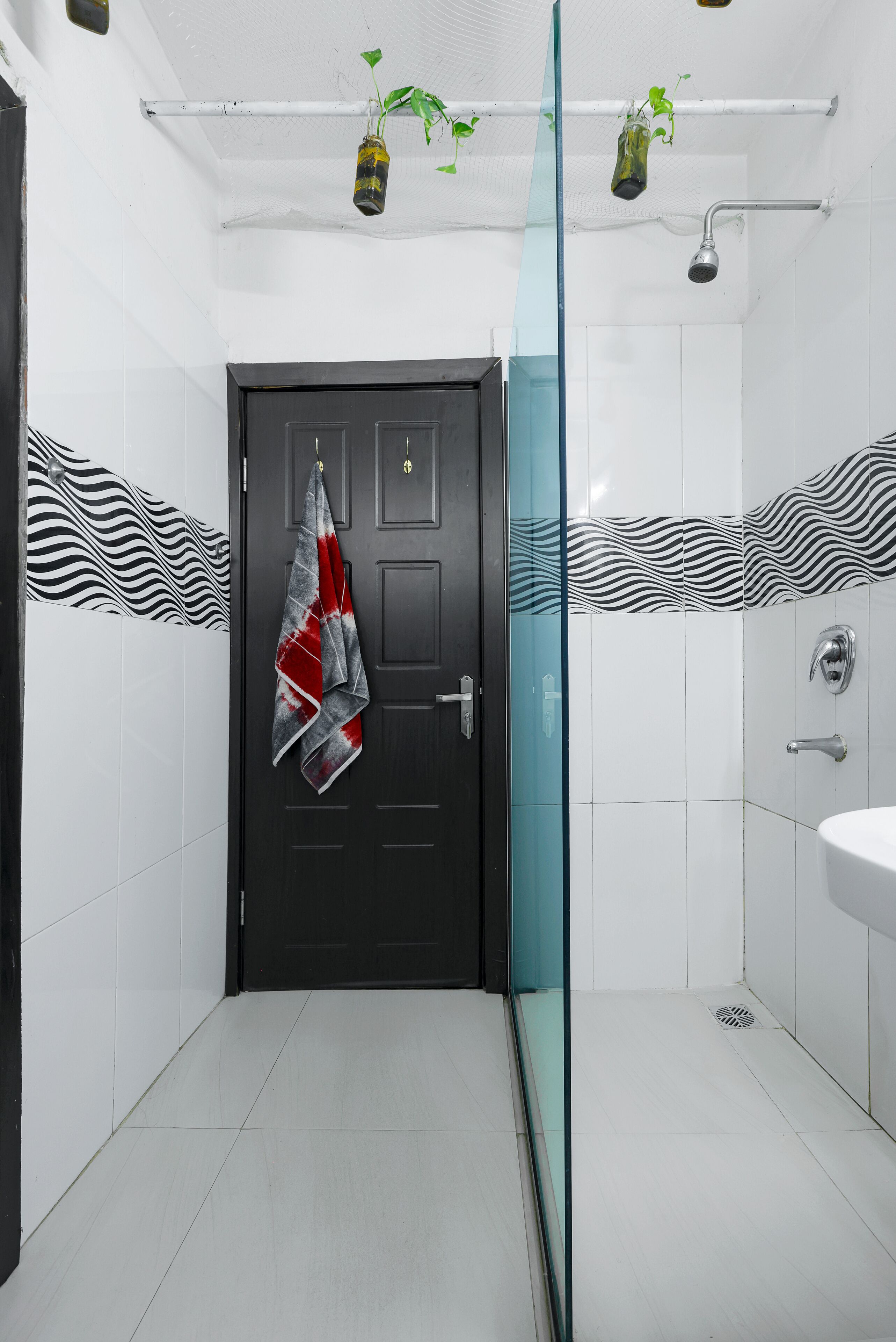Un baño con puerta negra, baldosas blancas, cabina de ducha de vidrio y una toalla colgada en la puerta.