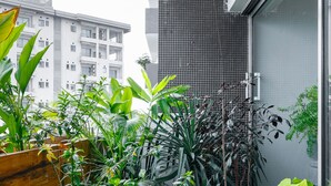 Un balcone con diverse piante in vaso, un fioriere in legno e vista su un edificio sullo sfondo.