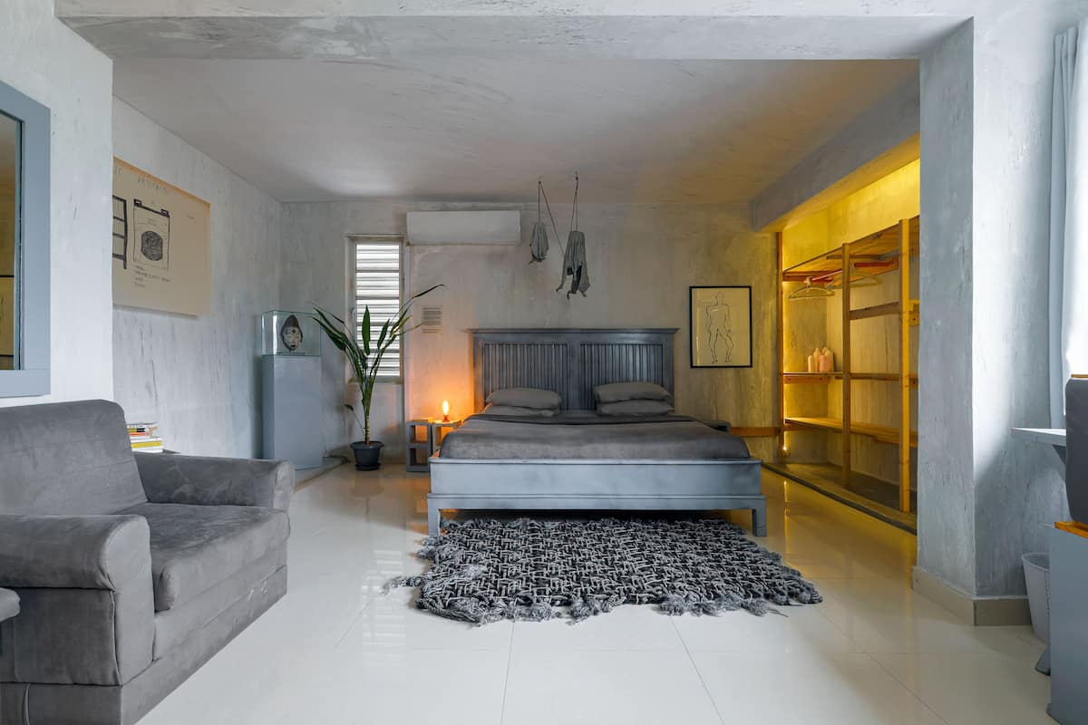A modern bedroom with a bed, a grey sofa, a rug, and a wardrobe.
