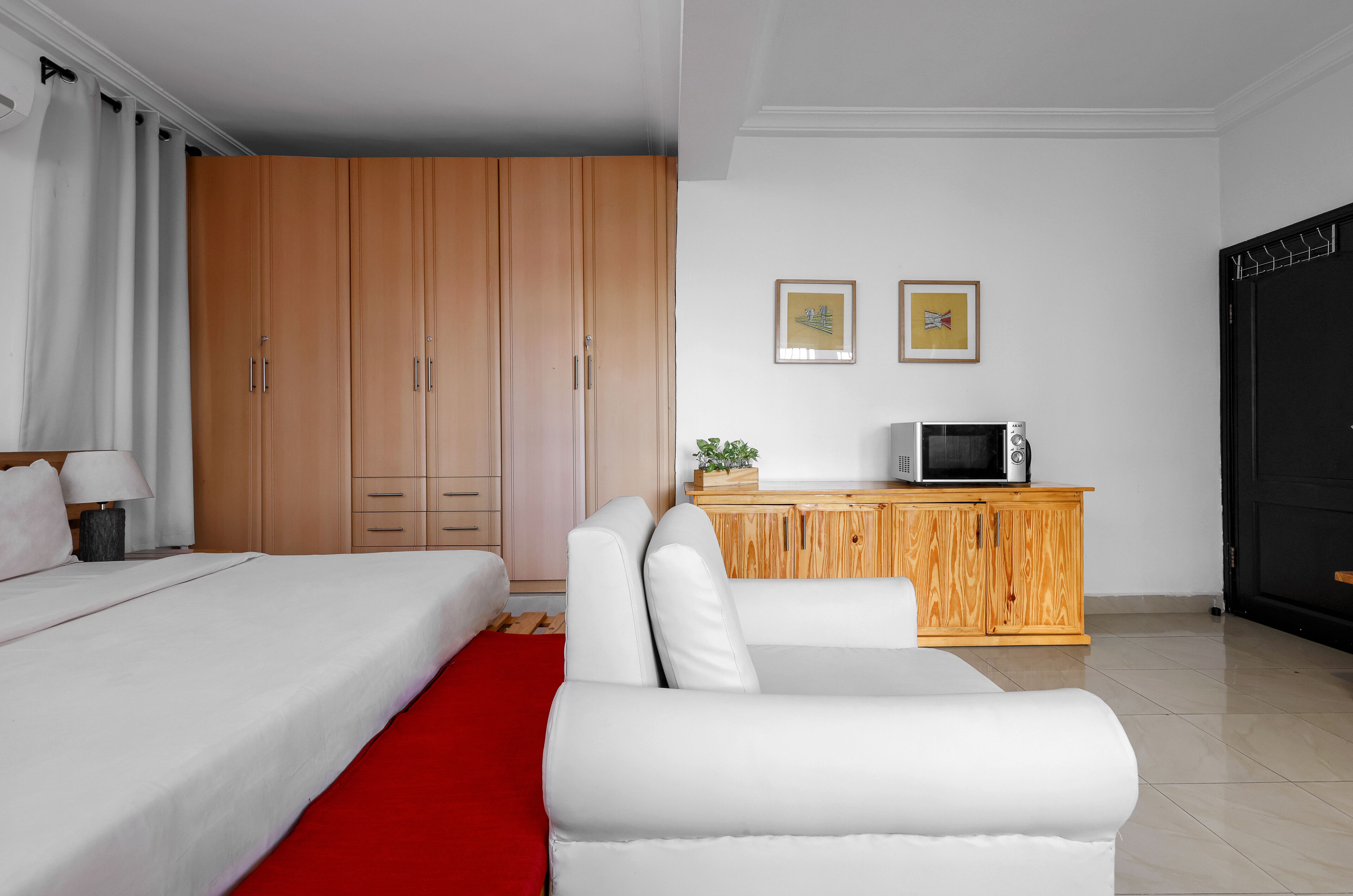 A hotel room with a bed, a white sofa, a wooden cabinet with a TV, and a red rug.