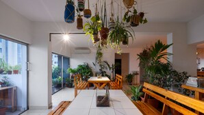 Zona pranzo moderna con tavolo e panche in legno, circondata da piante in vaso e fioriere pensili.